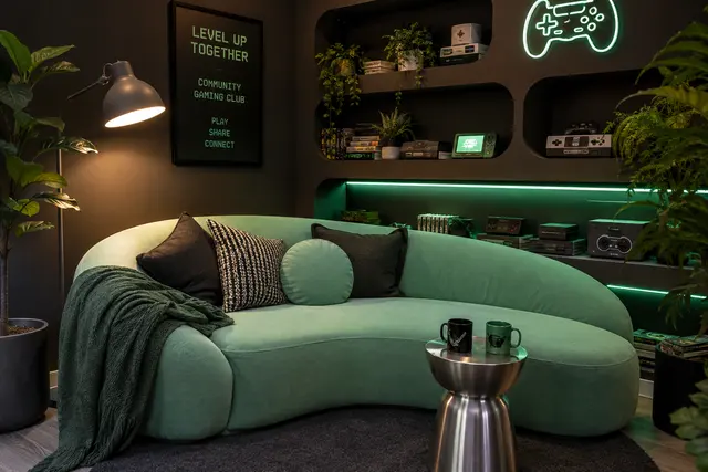 Sofá curvo color menta con luces led verdes y repisas con consolas retro en el lounge del Hub