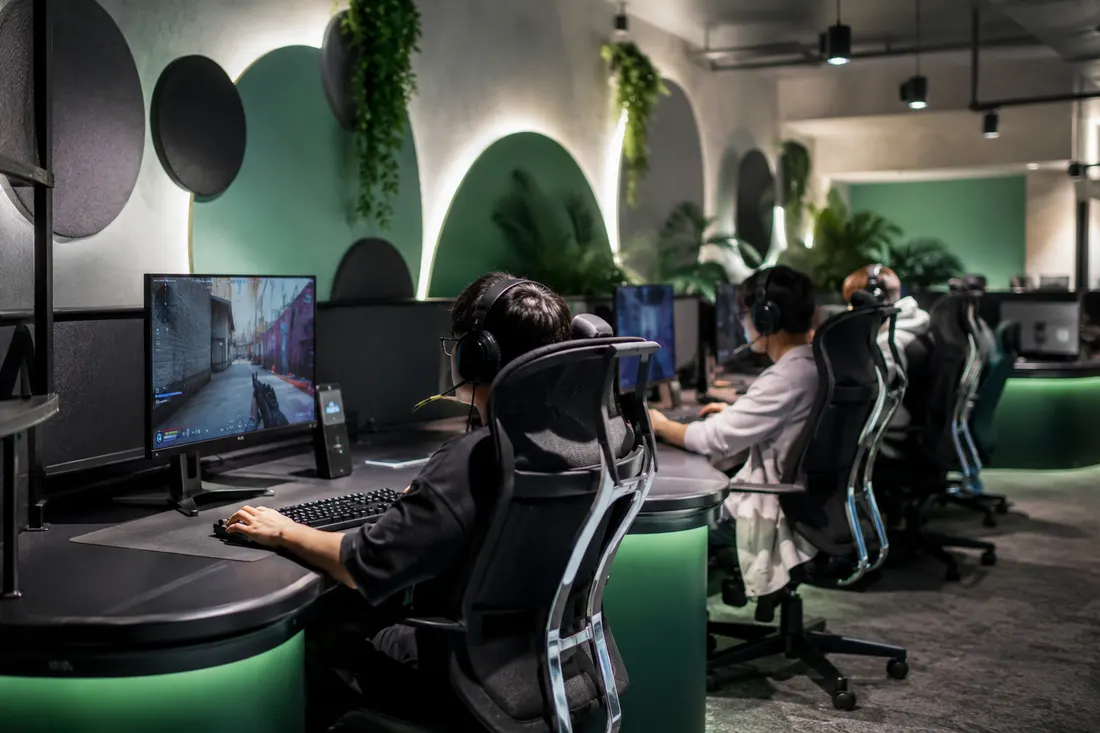 Fila de PC gamer con monitores encendidos y luces verdes en los escritorios del Hub